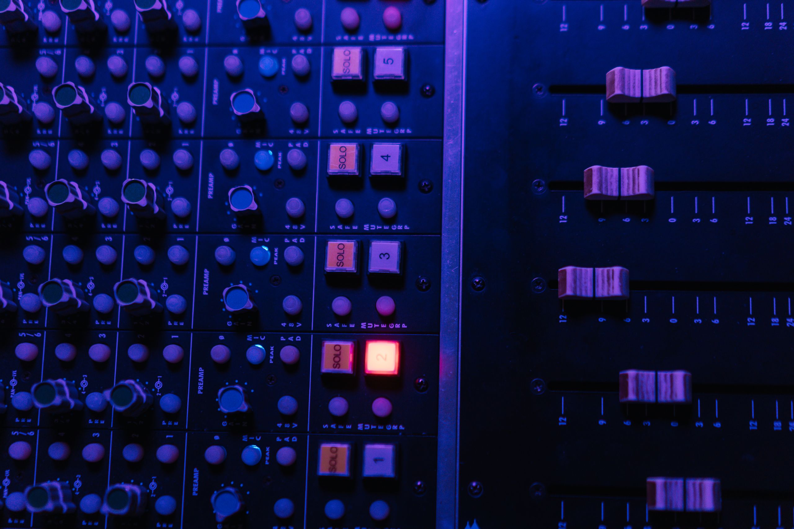 Detailed view of an audio mixing console with glowing buttons and sliders under ambient lighting.